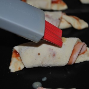 Vzniknutú pizzu rozdelíme na 8 častí zvinieme a ukladáme na plech. Potrieme rozšľahaným žĺtkom a dáme upiecť do rúry.