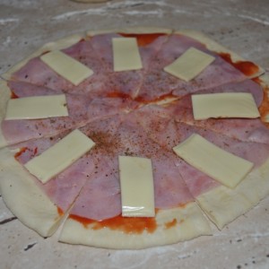 Cesto vyvaľkáme, potrieme kečupom, posypeme pizza korením, pridáme šunku, syr (prípadne olivu, klobásku) každému podľa chuti.