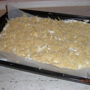 2/3 odležaného cesta vyvaľkáme na plán a dáme na vymastený plech.  Jablkovú hmotu rozložíme na cesto, Z bielkov, 100g krupicového cukru a  citronovej šťavy vyšlaháme tuhý sneh a rozotrieme na jablkovú plnku.  Cesto z mrazničky nahrubo nastrúhame na sneh.